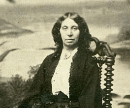 Woman wearing full skirt and blouse sits with a large dog to her right. Woman wearing full skirt and blouse sits with a large dog to her right.